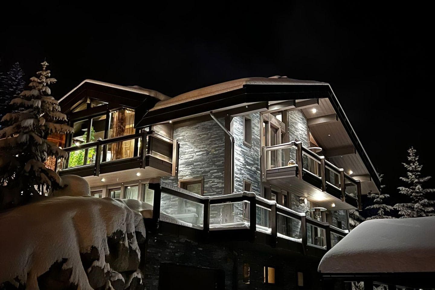 Chalet exterior at night with multiple private balconies and stone facade