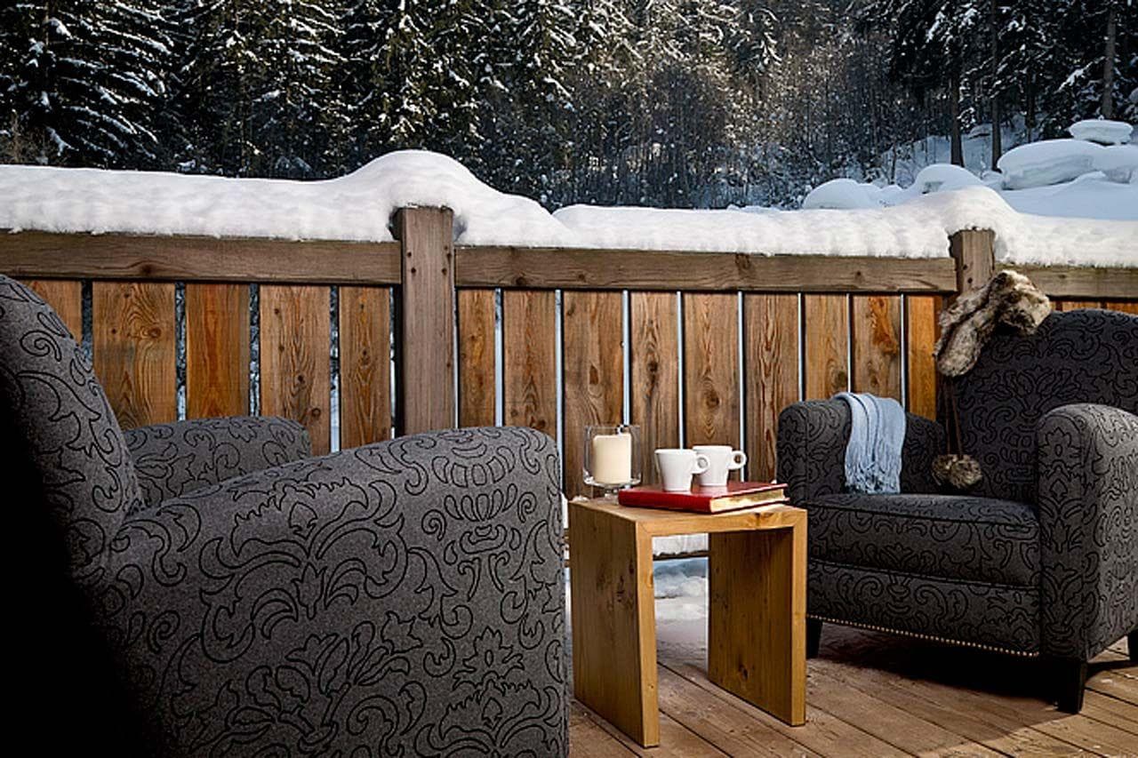 Private wooden deck with upholstered armchairs and forest views
