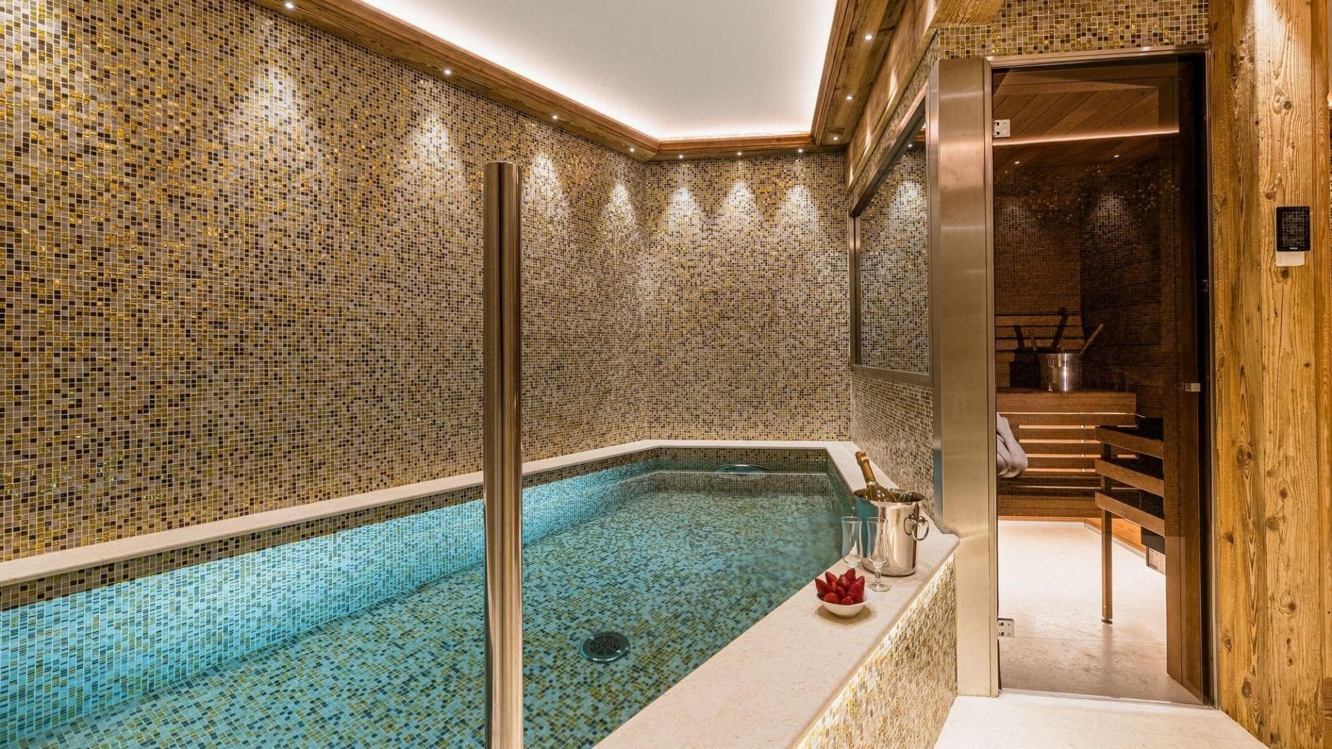 Indoor plunge pool with gold mosaic tiling and adjacent wood-lined sauna