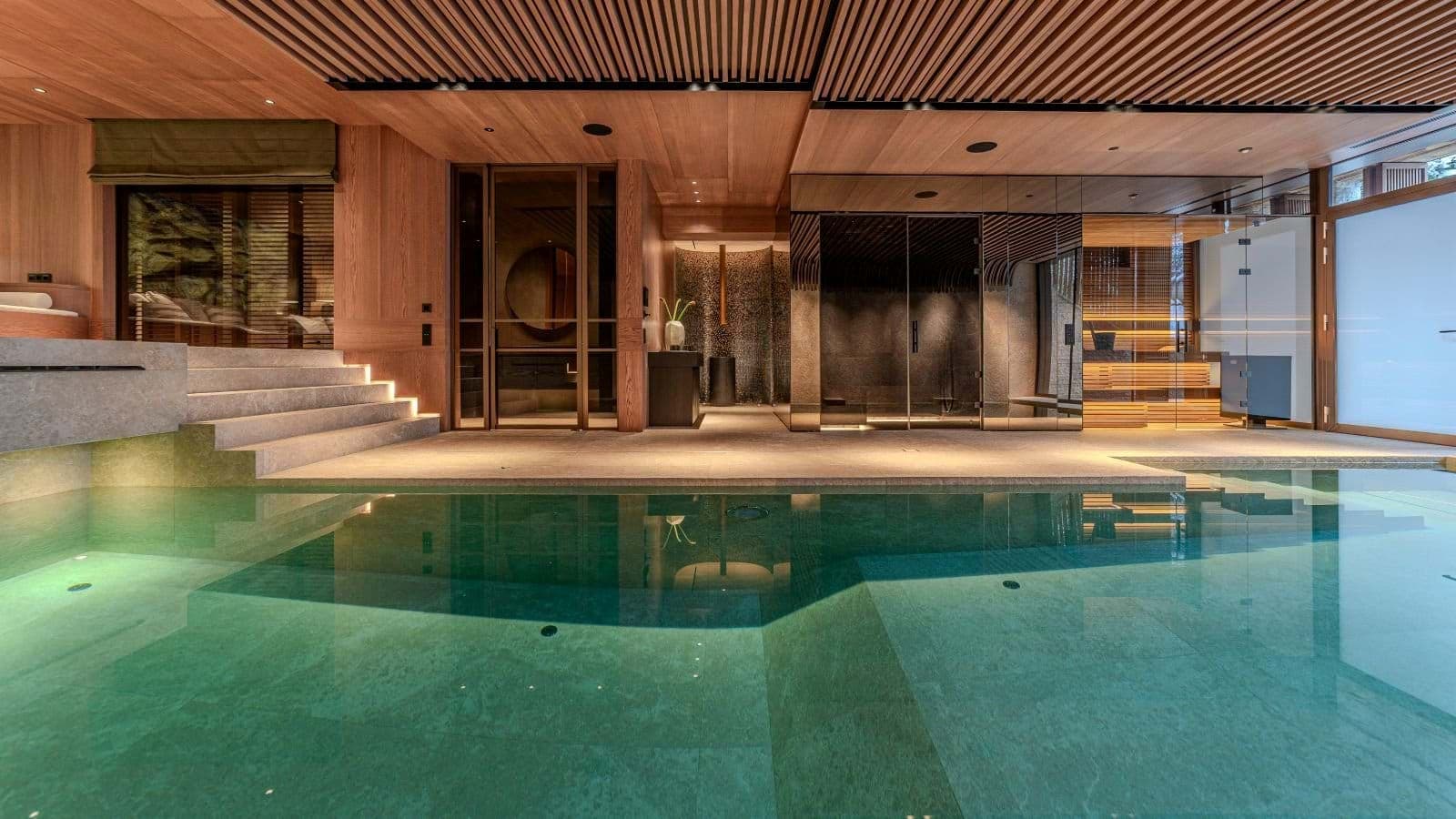 Indoor pool and spa area with glass-walled sauna and steam room
