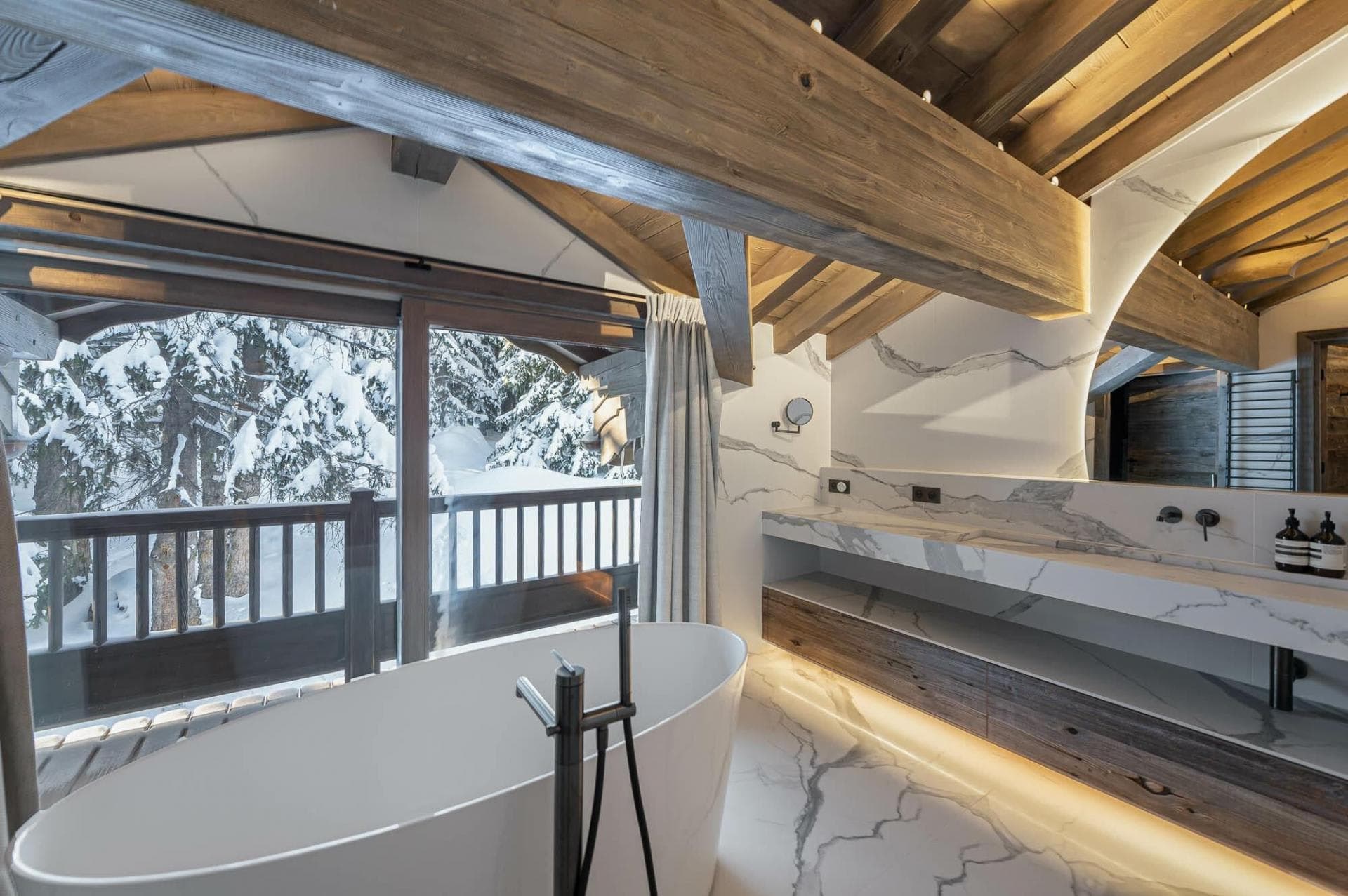 Bathroom with freestanding tub and balcony overlooking snowy forest