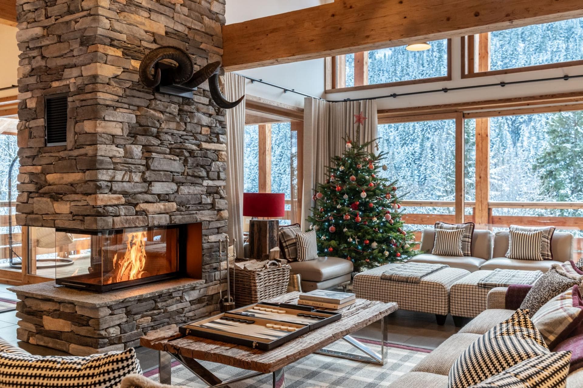 Living area with three-sided stone fireplace and snow-covered forest views