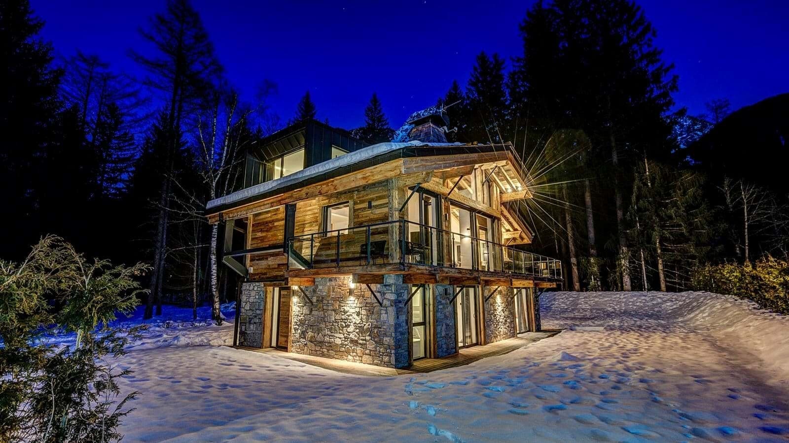 Chalet exterior with stone base and wrap-around balcony at night