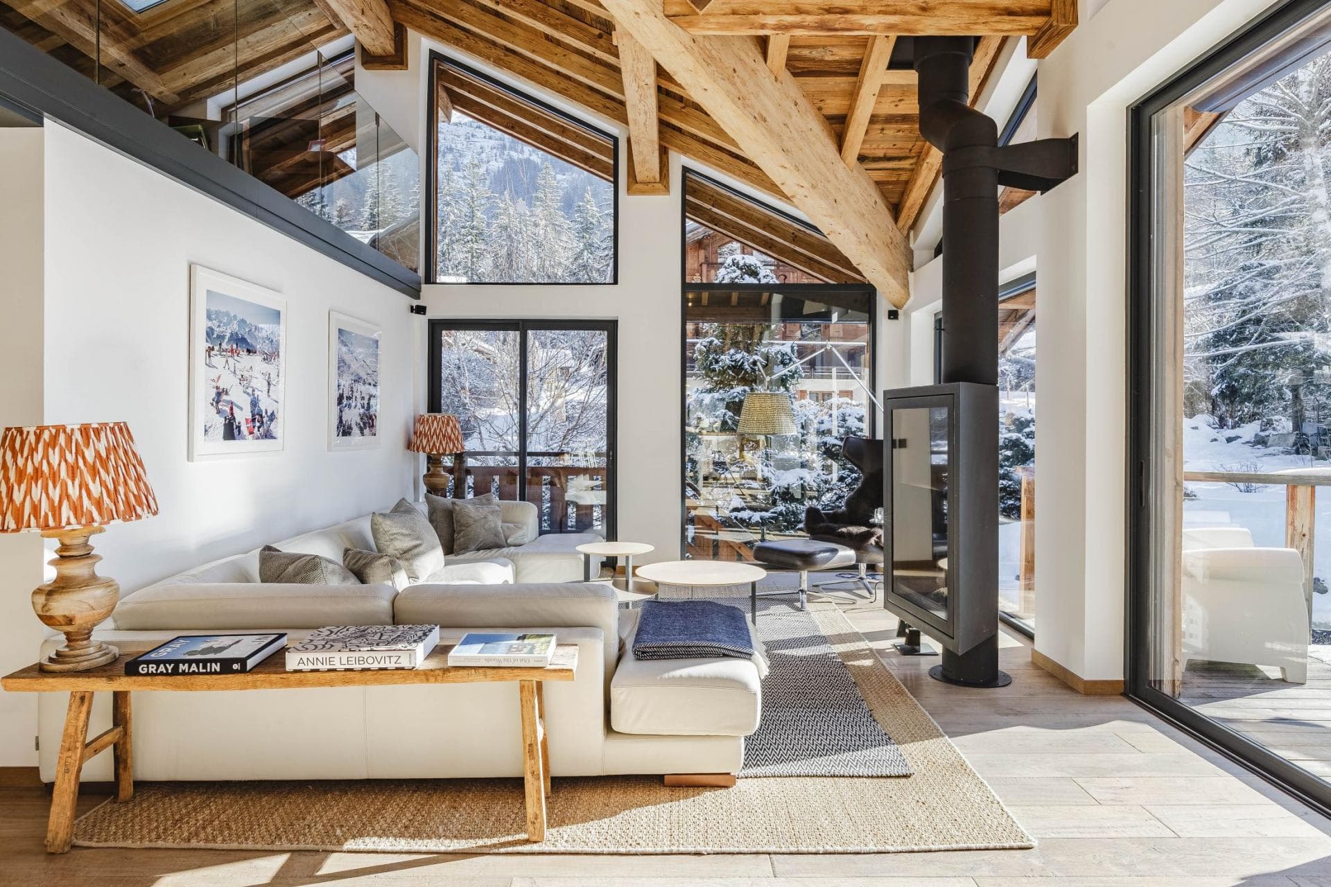 Living room with wood beam ceiling, wood-burning stove, and floor-to-ceiling windows overlooking snowy landscape