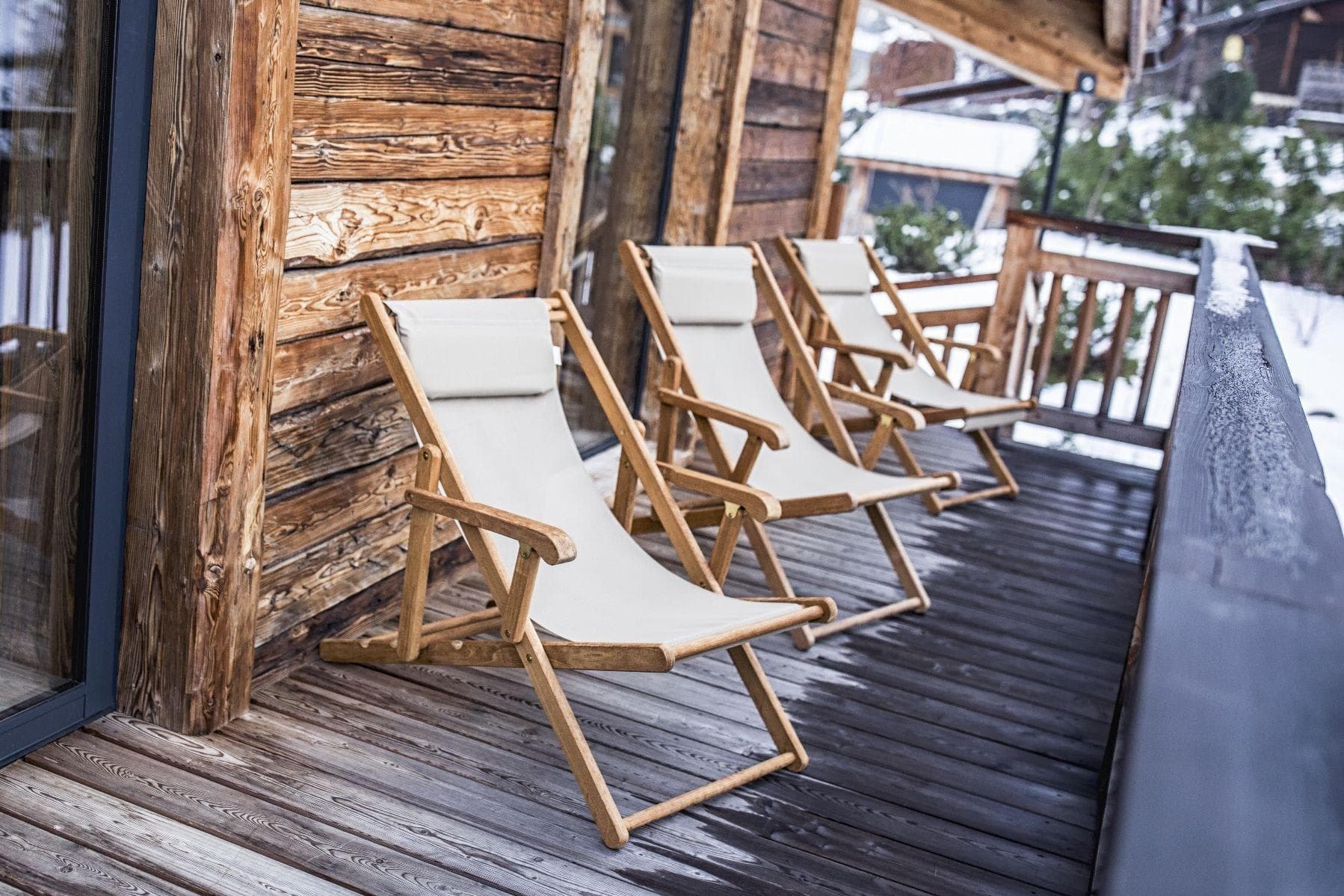 Wooden balcony with three reclining deck chairs and snowy views