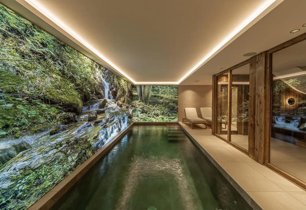 Indoor pool with forest mural beside a glass-fronted sauna