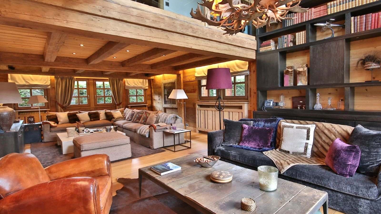 Double living area with antler chandelier, exposed beams, and library shelving