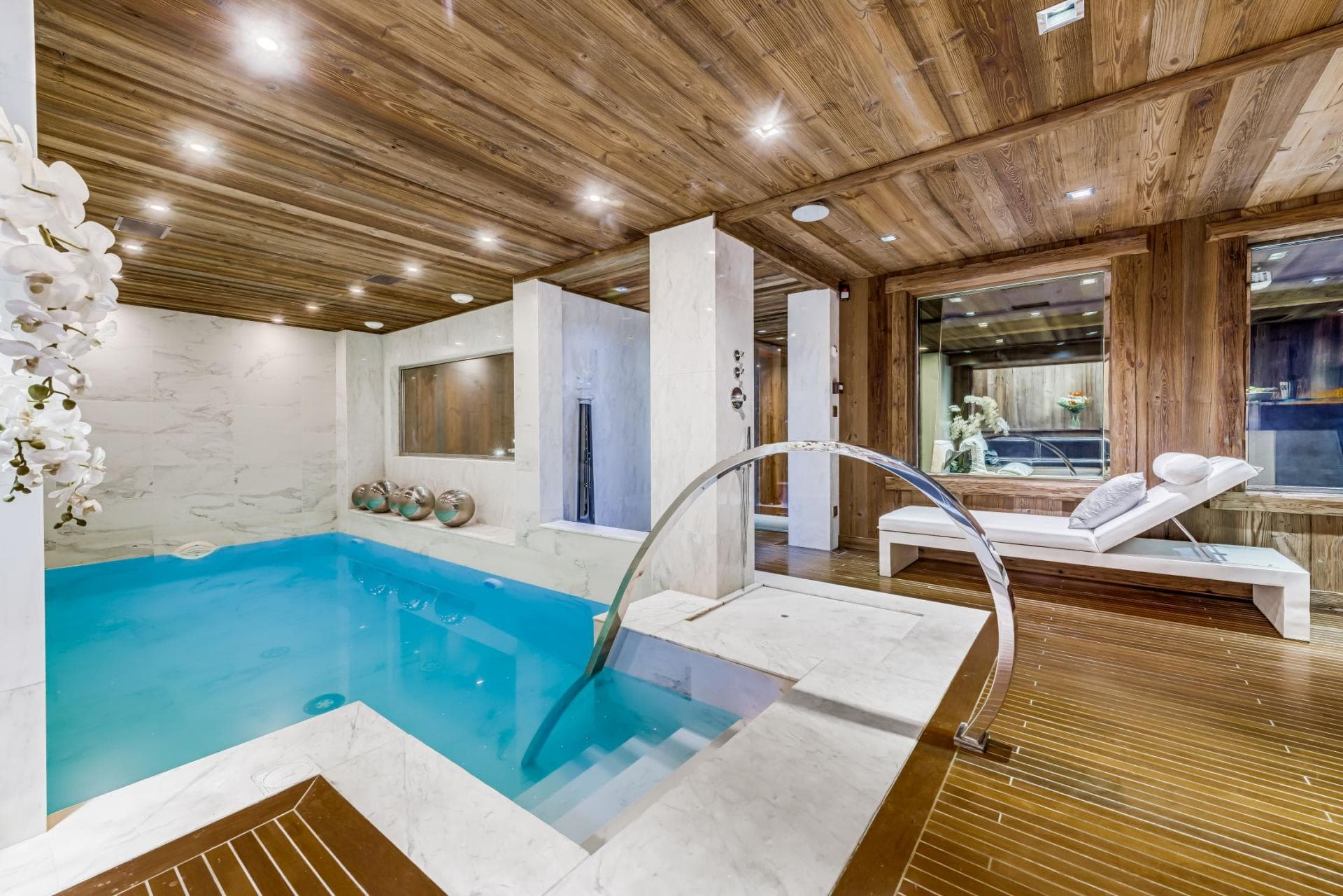 Indoor heated pool with marble steps and poolside lounge seating