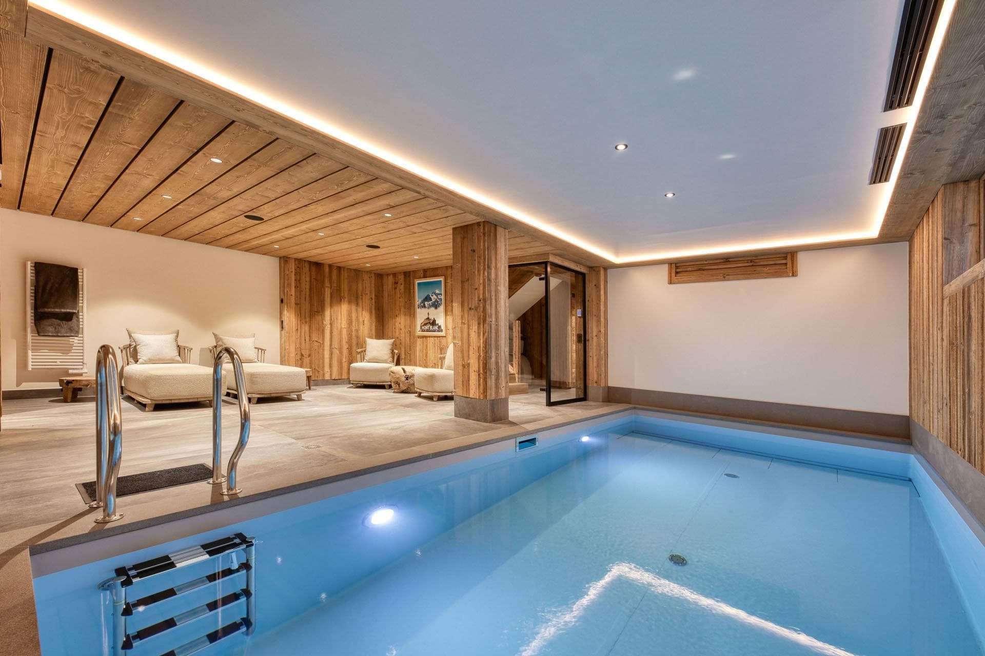 Indoor swimming pool with heated water and lounge seating; wood-beamed ceiling