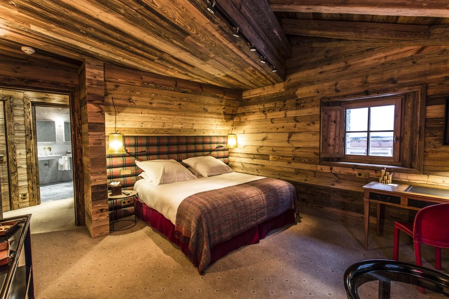 Wood-paneled bedroom with queen bed, ensuite bathroom, and desk area