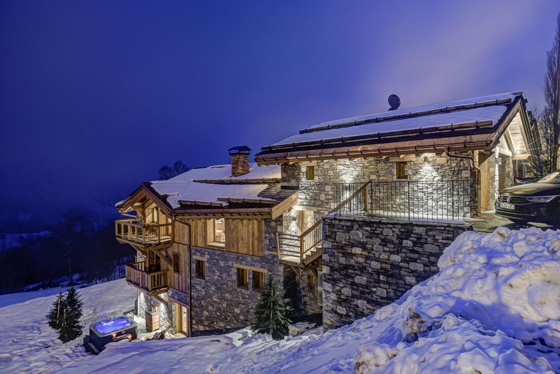 Stone chalet exterior with private driveway parking and outdoor hot tub