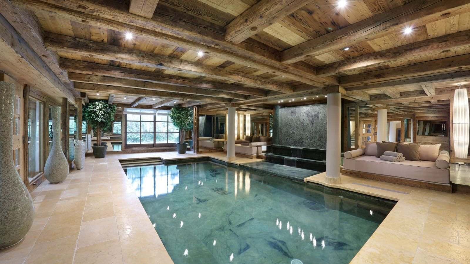 Indoor pool with waterfall feature and poolside daybed seating