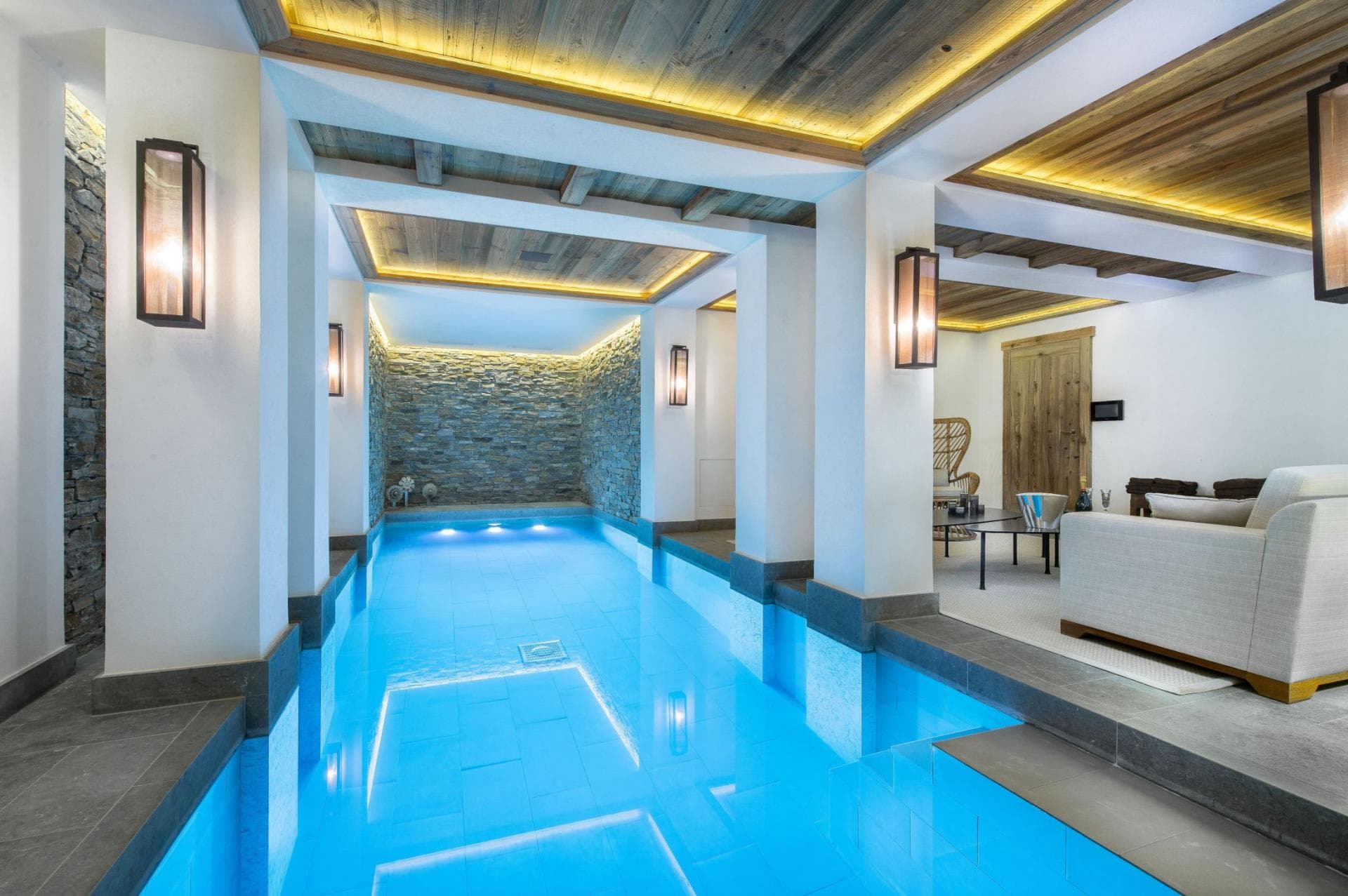 Indoor pool with underwater lighting and stone accent wall; connects to living area