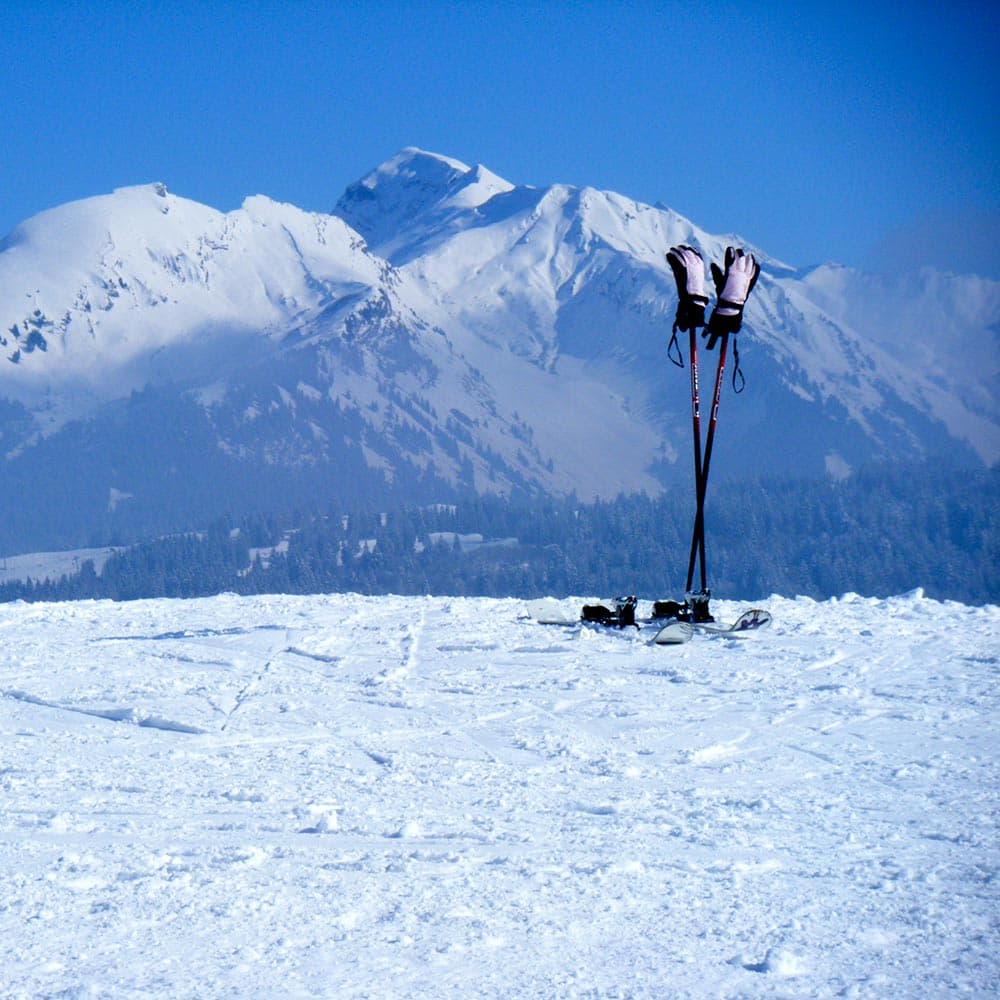 Skis and boots planted in snow with snow-covered alpine peaks backdrop