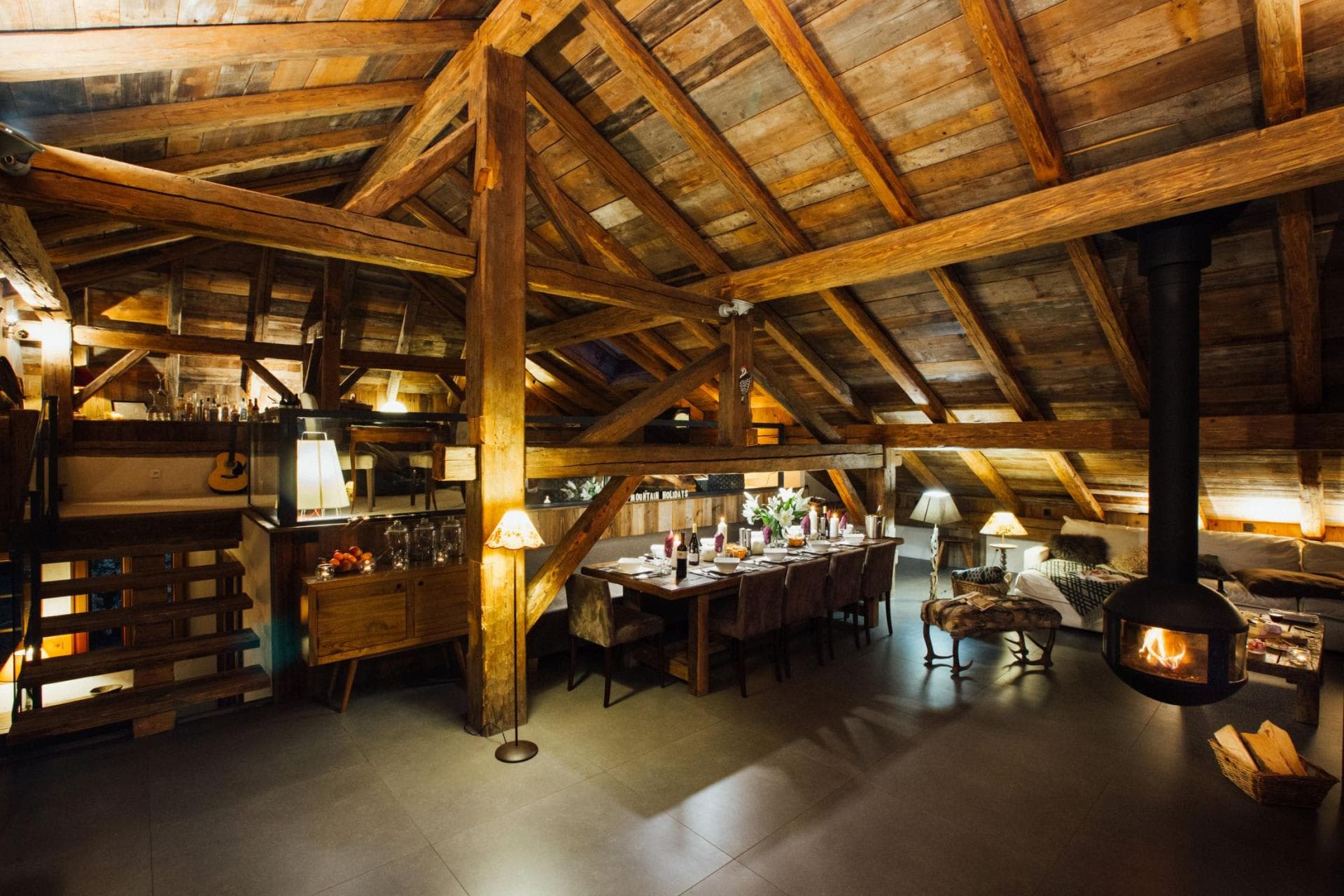 Open-plan dining area seats 10 under original timber beams with hanging fireplace