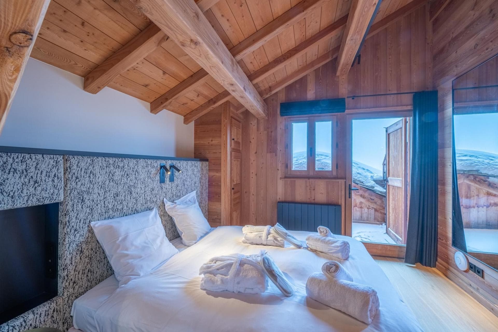 Bedroom with vaulted wood ceilings and direct balcony access to snowy views