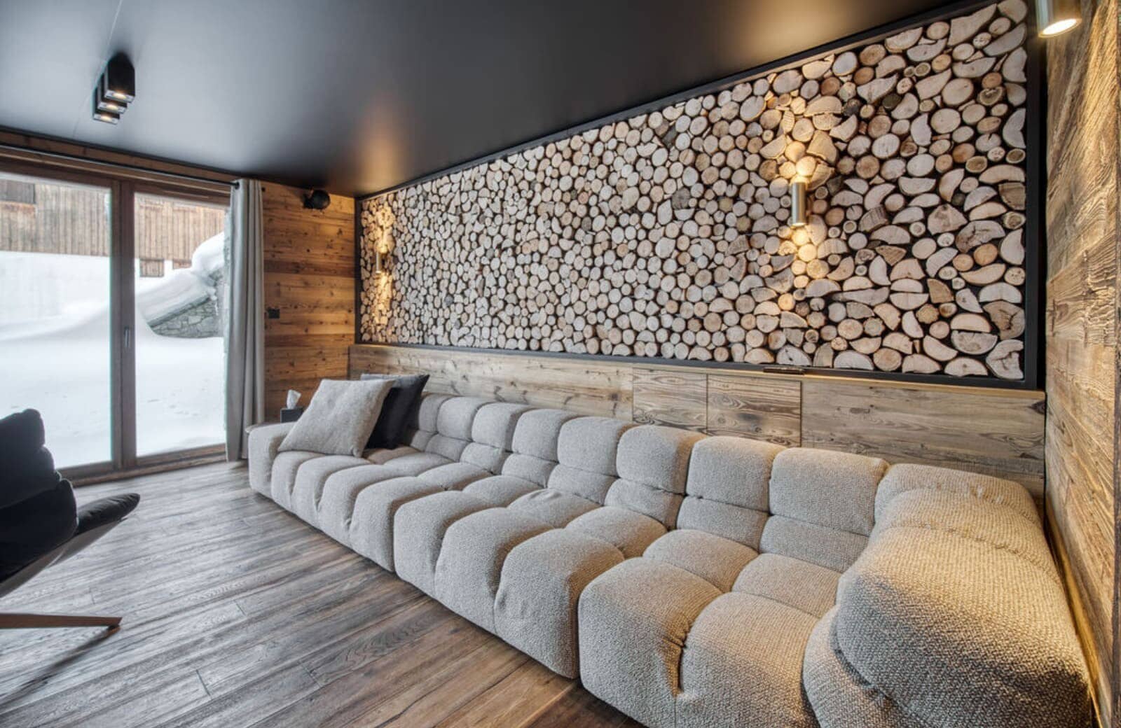 Media room with modular sofa and decorative log wall; terrace access