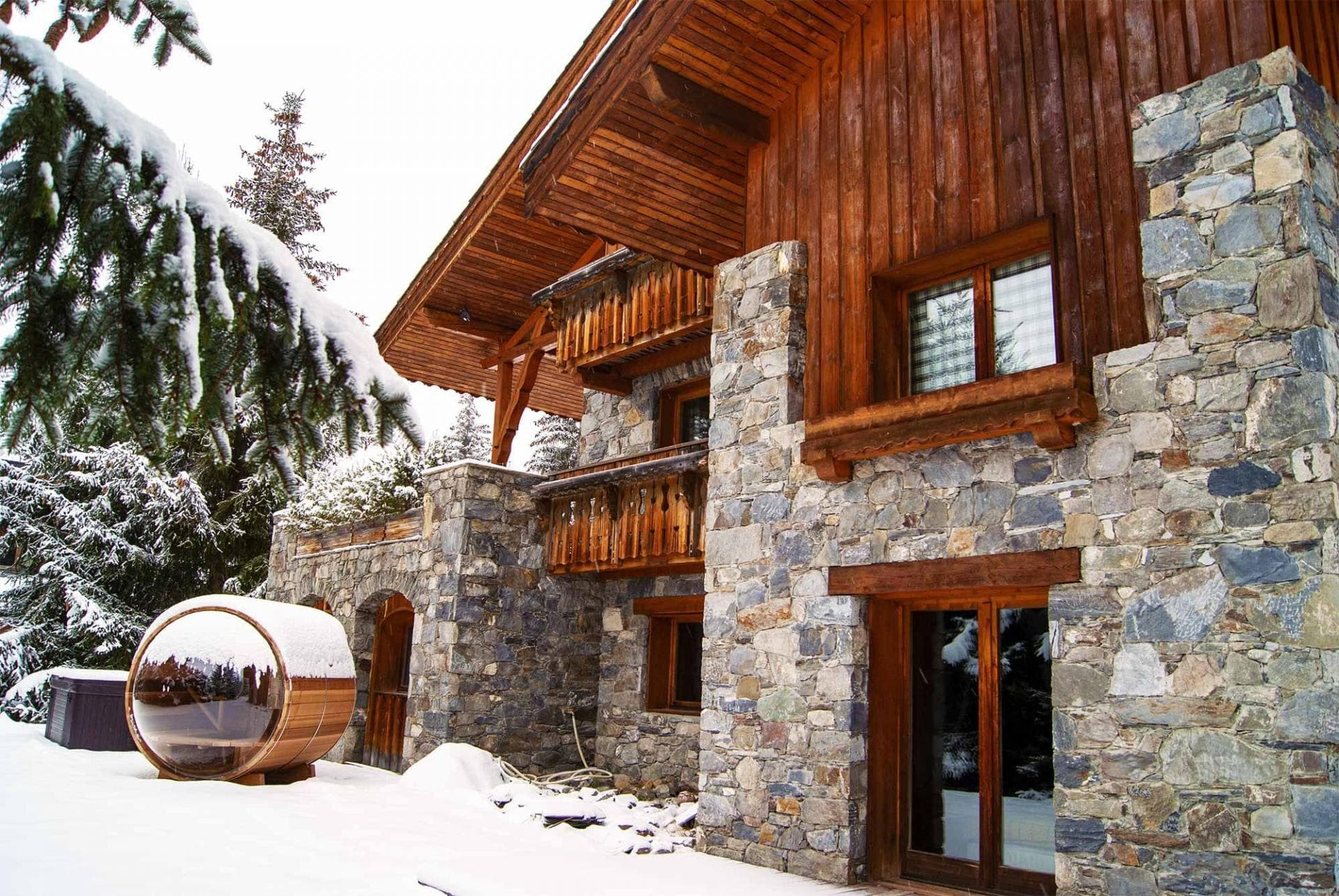 Stone-clad chalet exterior featuring outdoor barrel sauna and private balconies