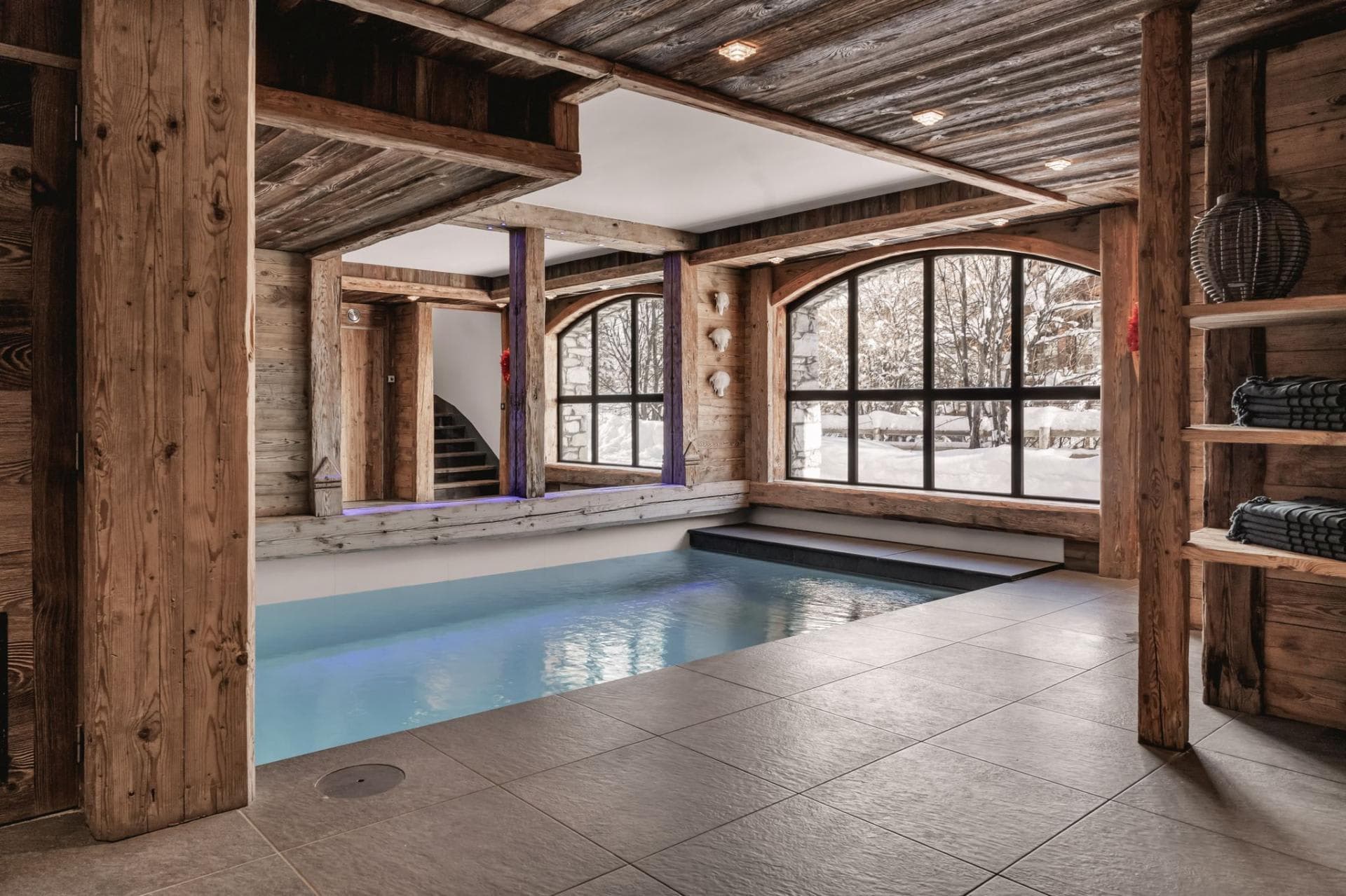 Indoor heated pool with reclaimed wood paneling and snow-covered forest views