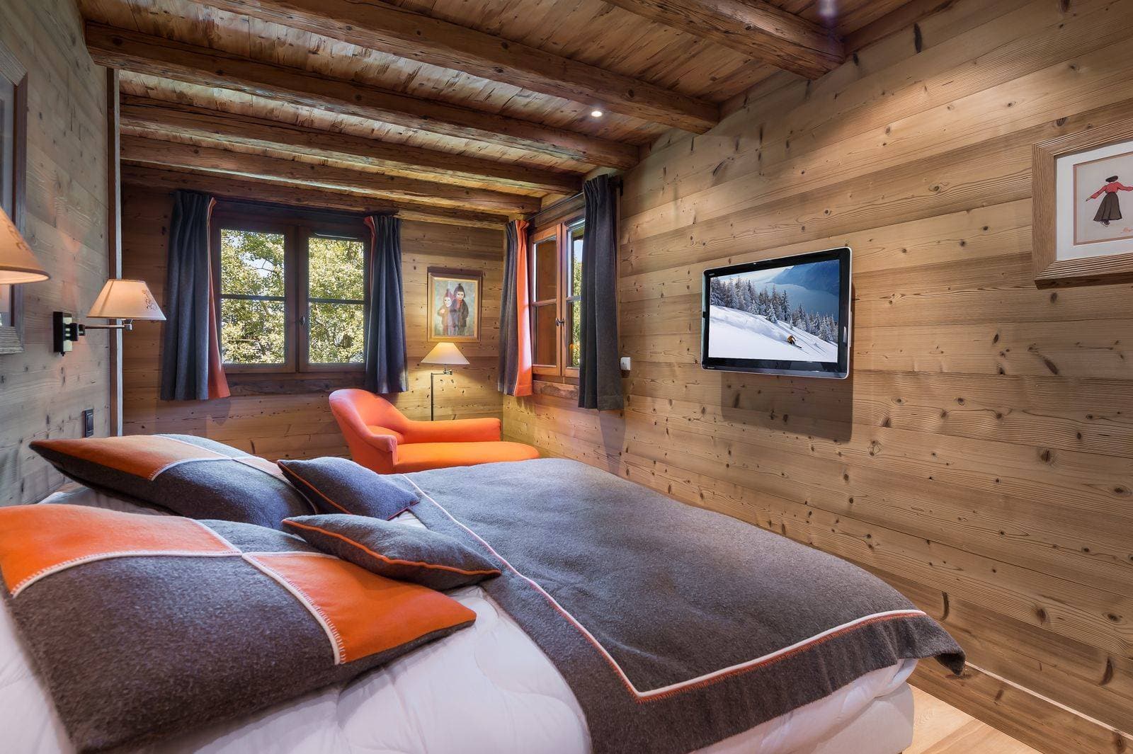 Wood-paneled bedroom with king bed, wall-mounted TV, and reading chaise