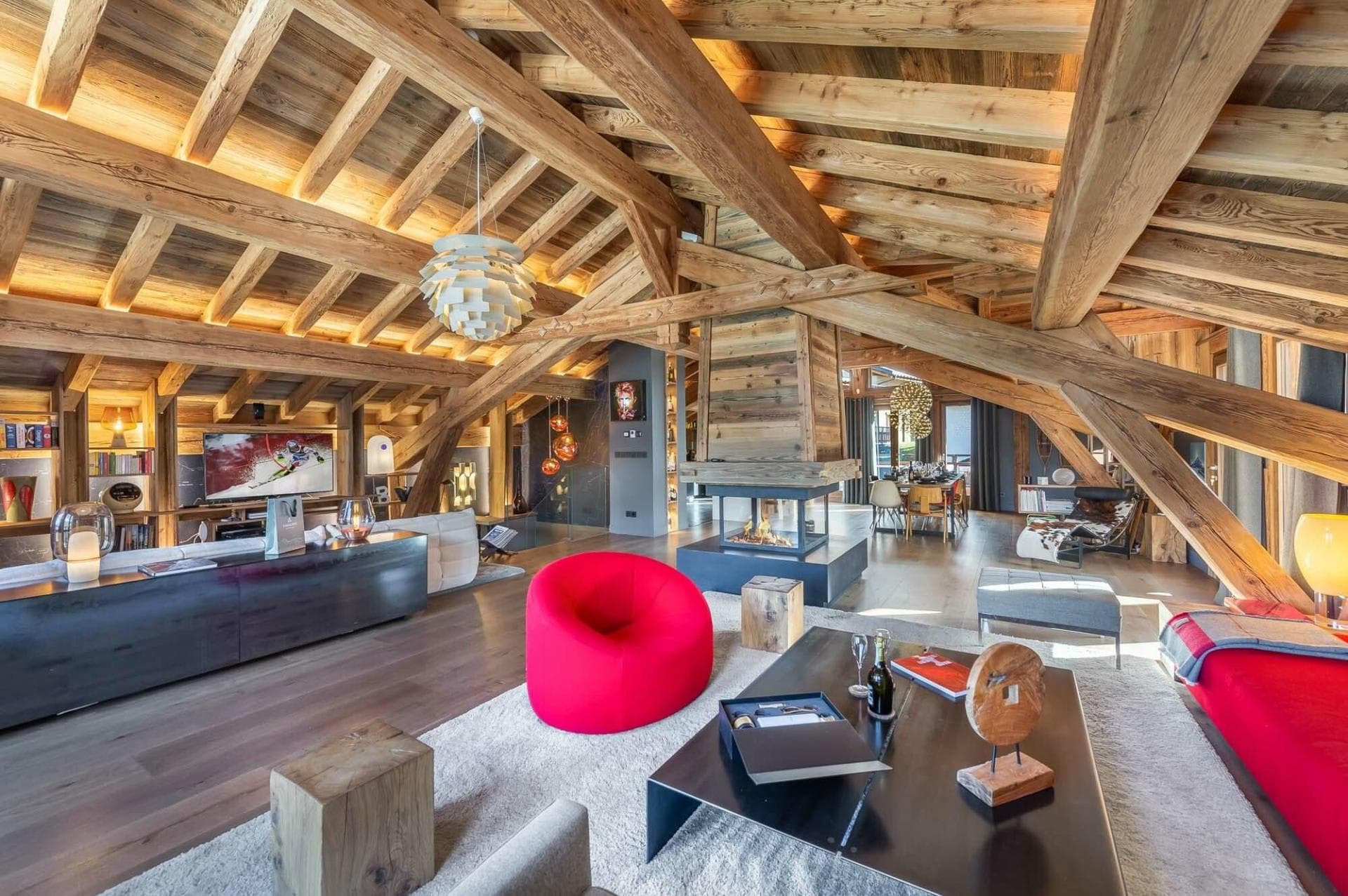 Open-plan living area featuring central 360-degree glass fireplace and vaulted timber ceilings