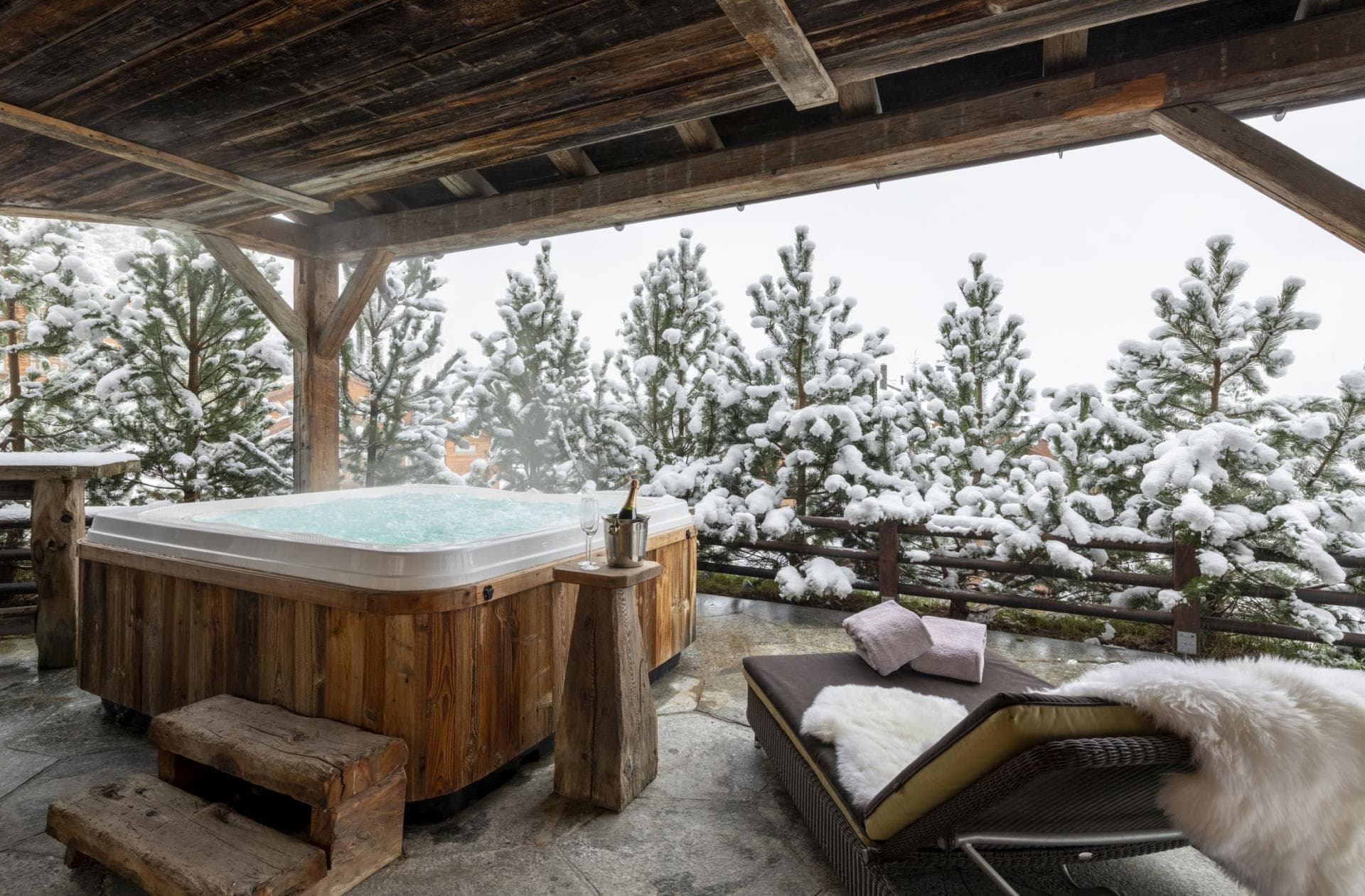 Covered outdoor hot tub with forest view and adjacent sun lounger