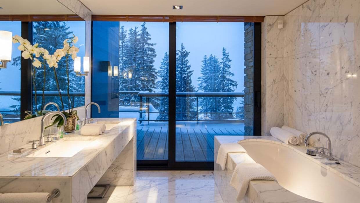 Bathroom with marble soaking tub and dual vanity; snowy forest view