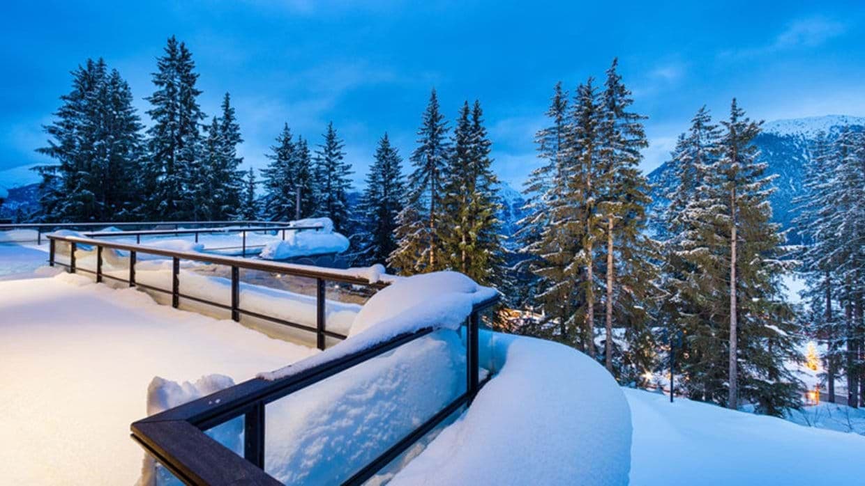Snow-covered terrace with glass railings and mountain forest views