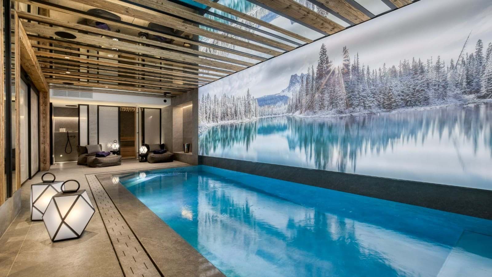 Indoor pool with alpine mural, backlit lanterns, and adjacent sauna access