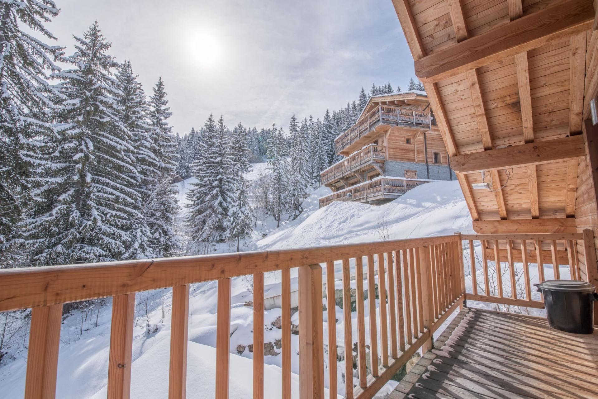 Covered wooden balcony with views of snowy forest and neighboring chalet