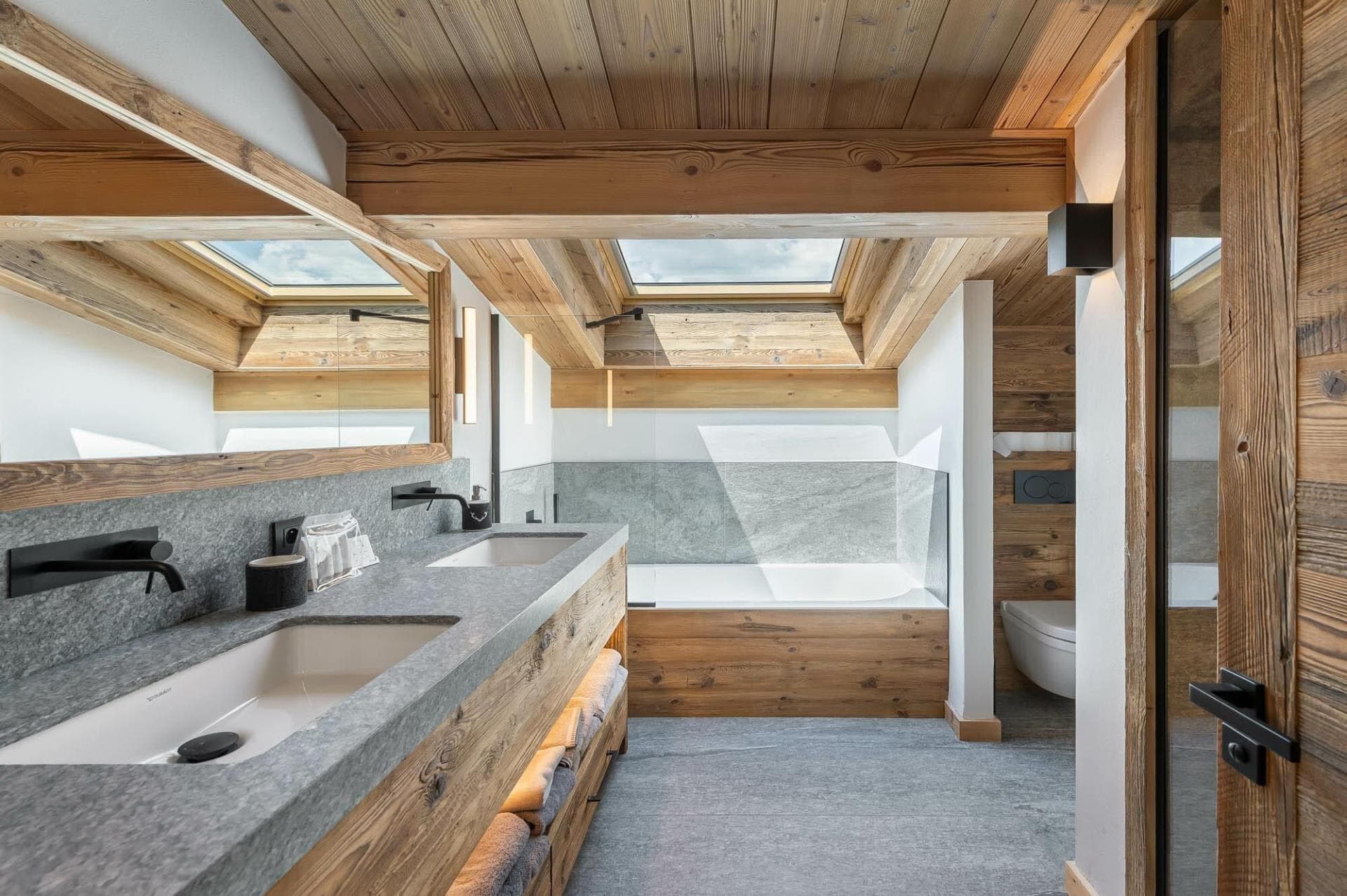 Bathroom with dual vanity, stone finishes, and soaking tub under skylight