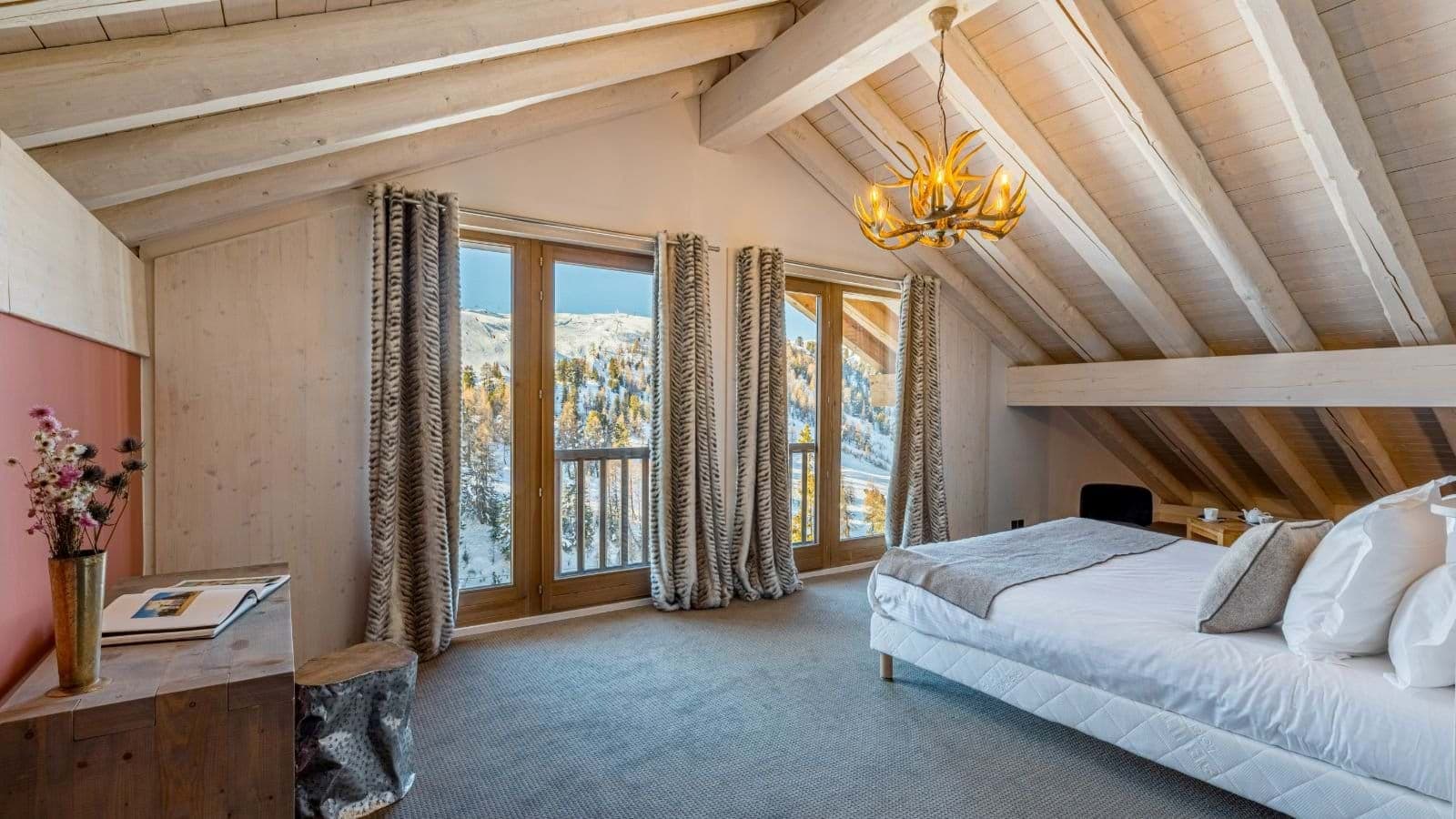 Top-floor bedroom with vaulted beam ceilings and mountain-view balcony