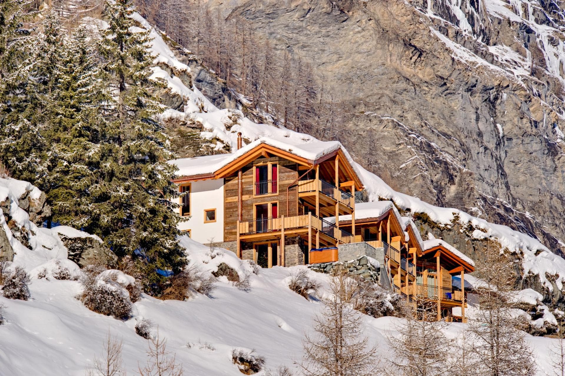 Ski-in chalet exterior featuring private balconies and mountain-view hot tub