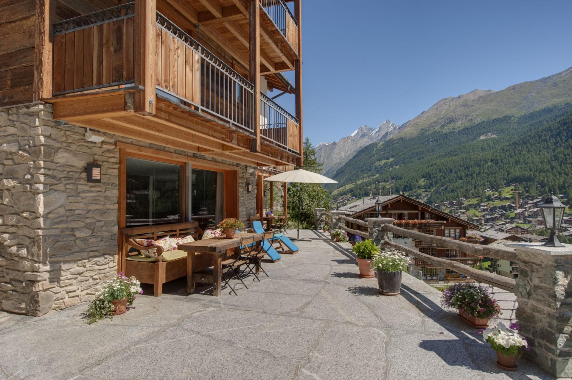 Stone terrace with dining table, sun loungers, and alpine valley views