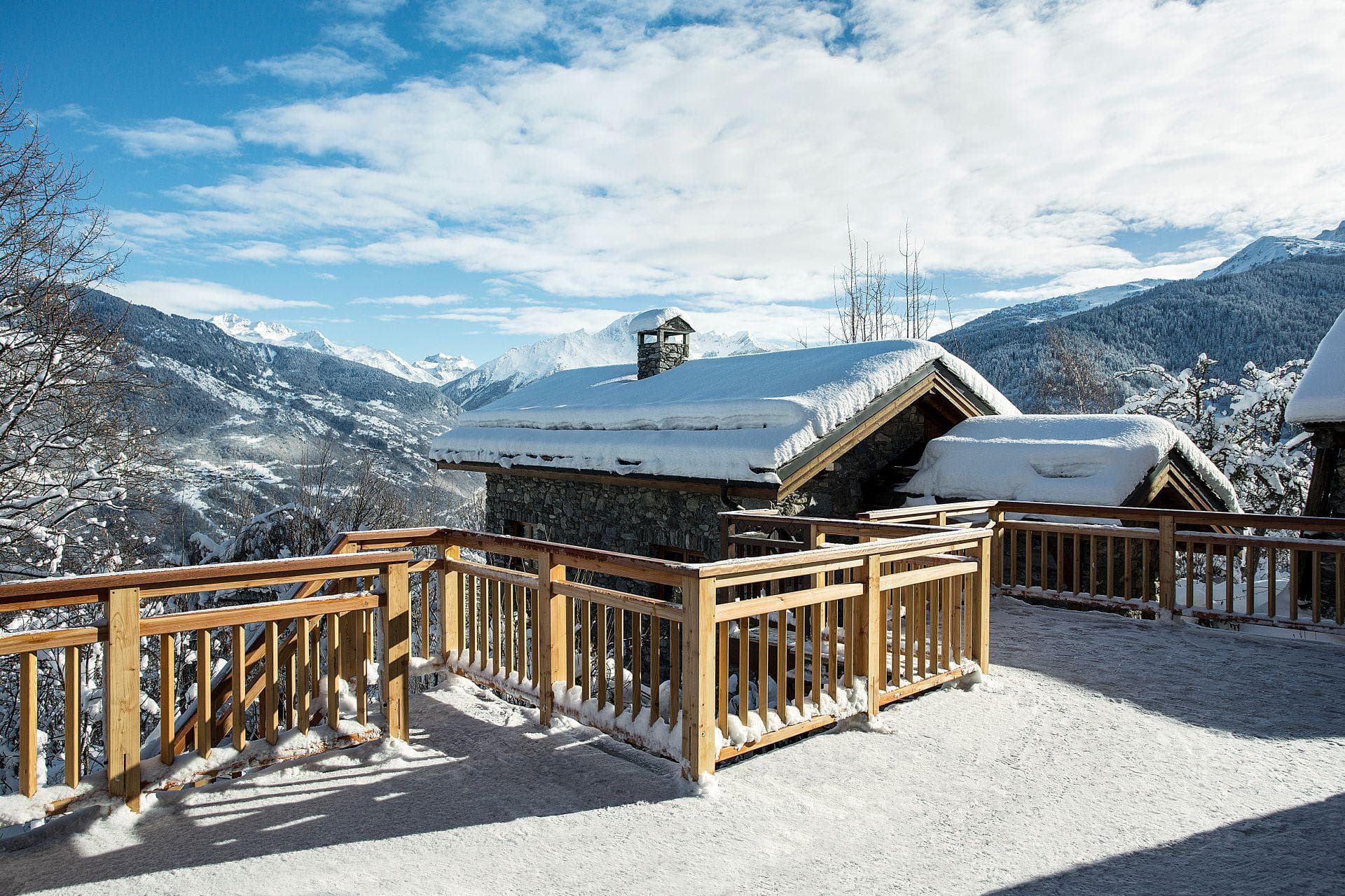 Stone chalet exterior with wrap-around sun deck and alpine valley views