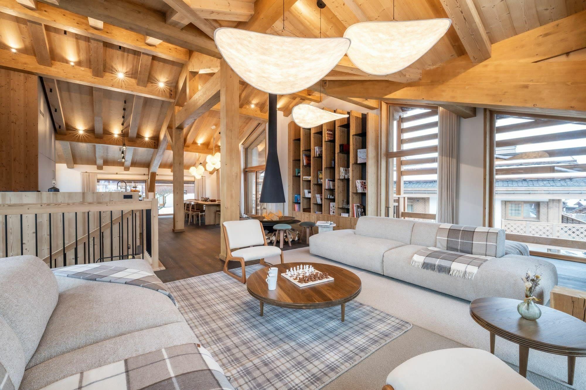Open-plan living room with curved sectional, wood beams, and full valley views through floor-to-ceiling windows