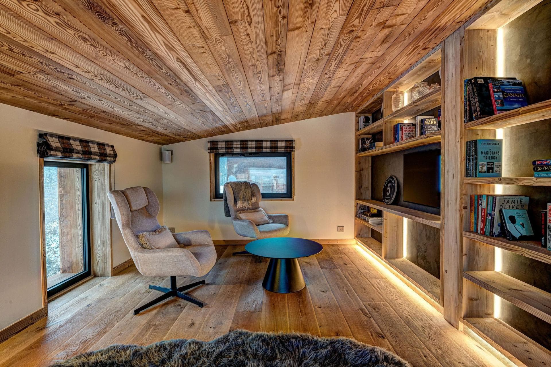 Library nook with swivel armchairs and backlit shelving; sloped wood ceilings