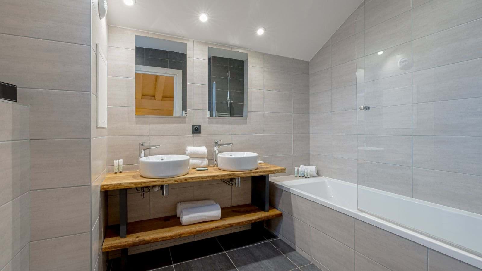 Bathroom with dual vessel sinks and bathtub with glass screen