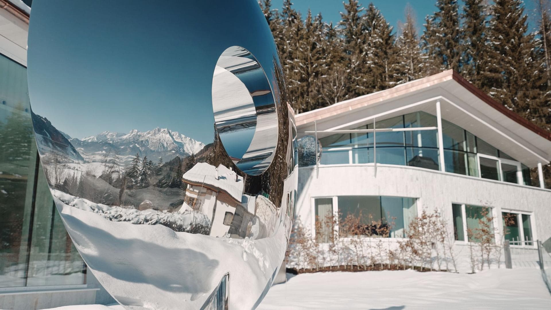 Chalet exterior featuring floor-to-ceiling windows and reflective mountain art sculpture