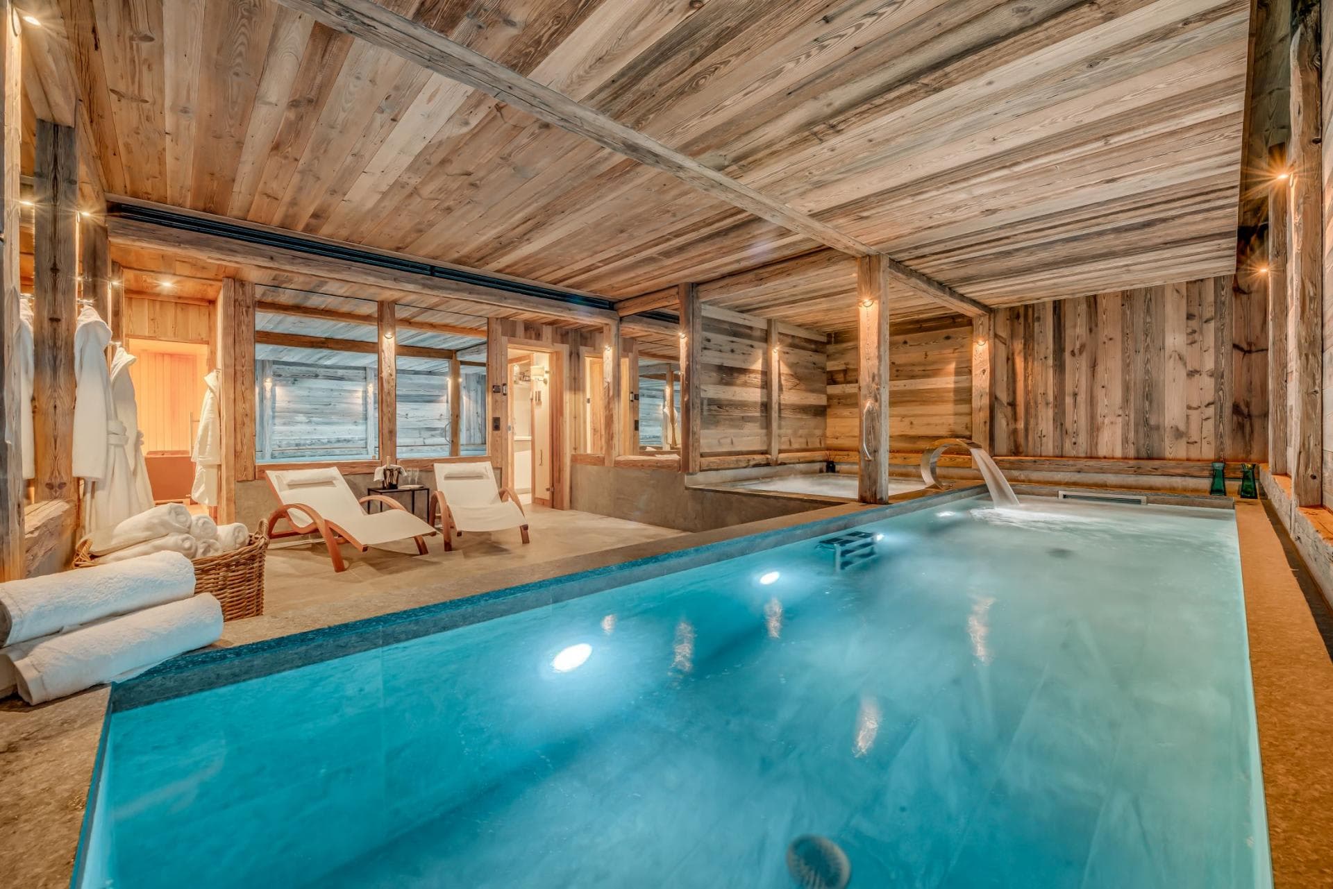 Indoor pool and hot tub area with adjacent wood-clad sauna