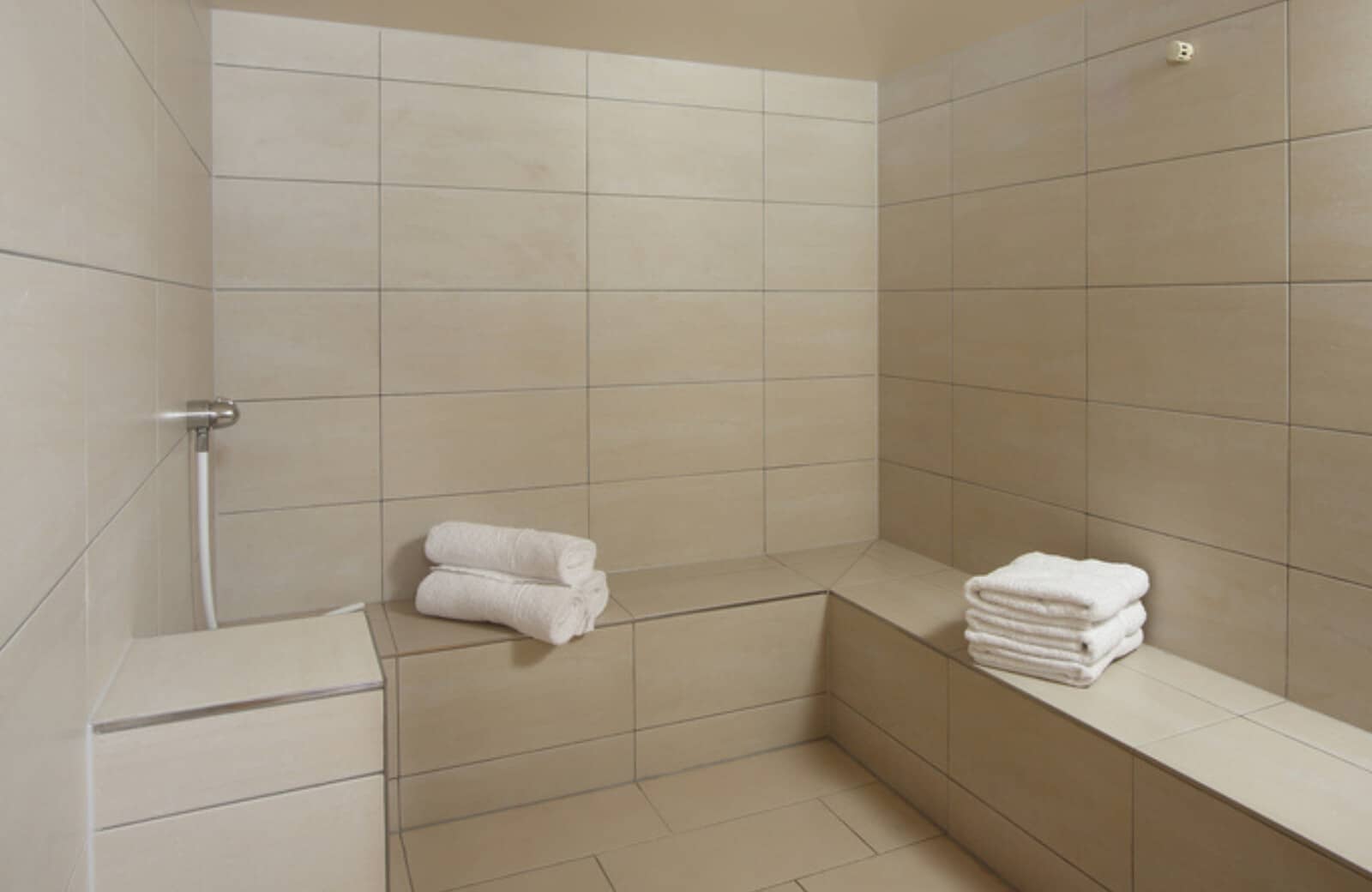 Private steam room with L-shaped bench seating and handheld sprayer