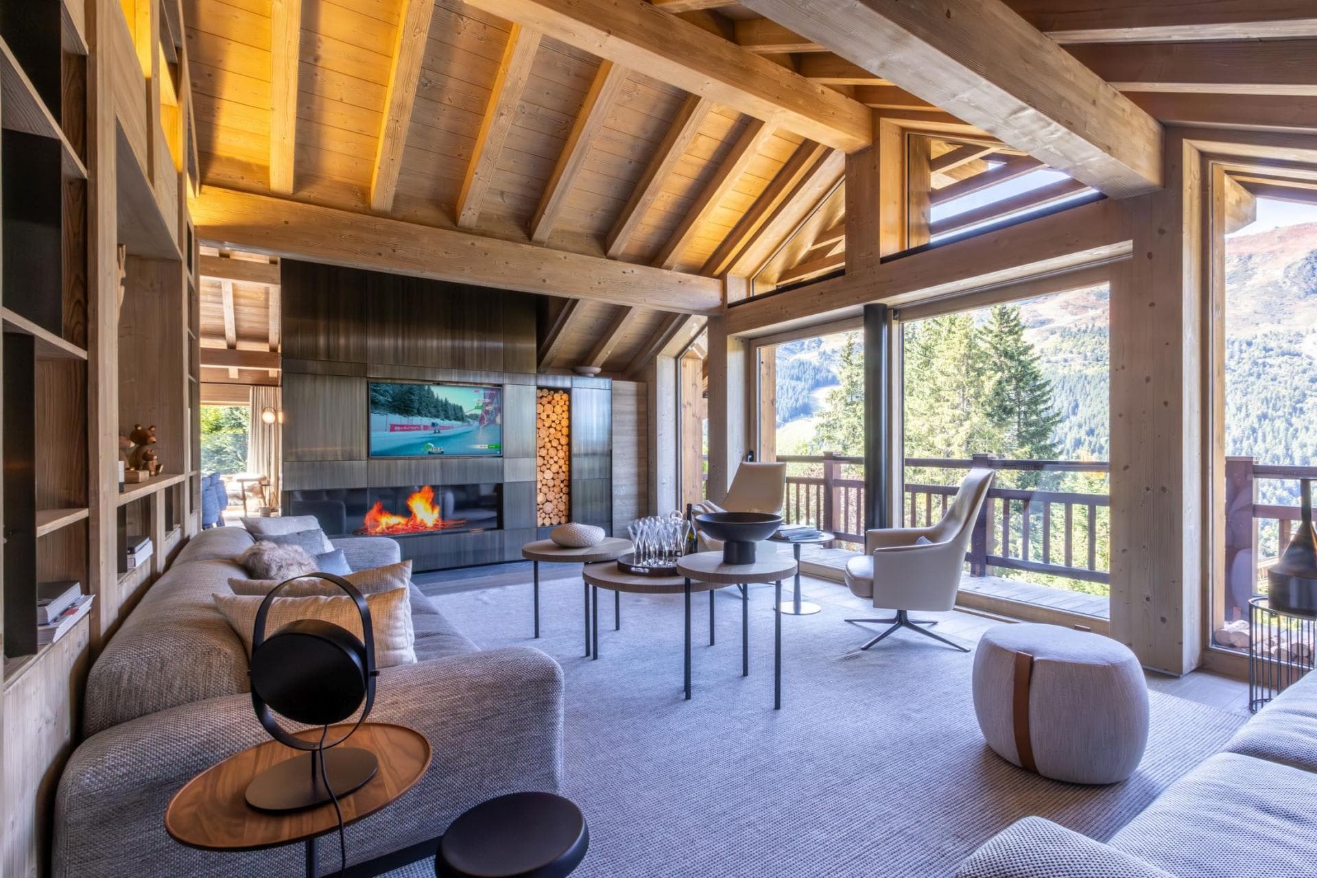 Living room with linear fireplace, timber beams, and floor-to-ceiling alpine views