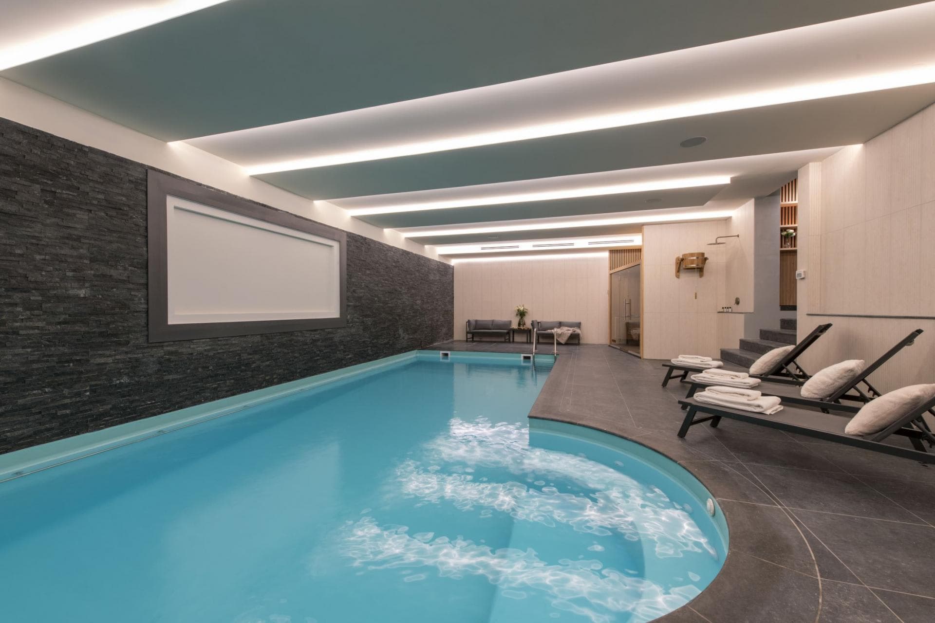 Indoor heated pool with sauna, rainfall shower, and lounge seating