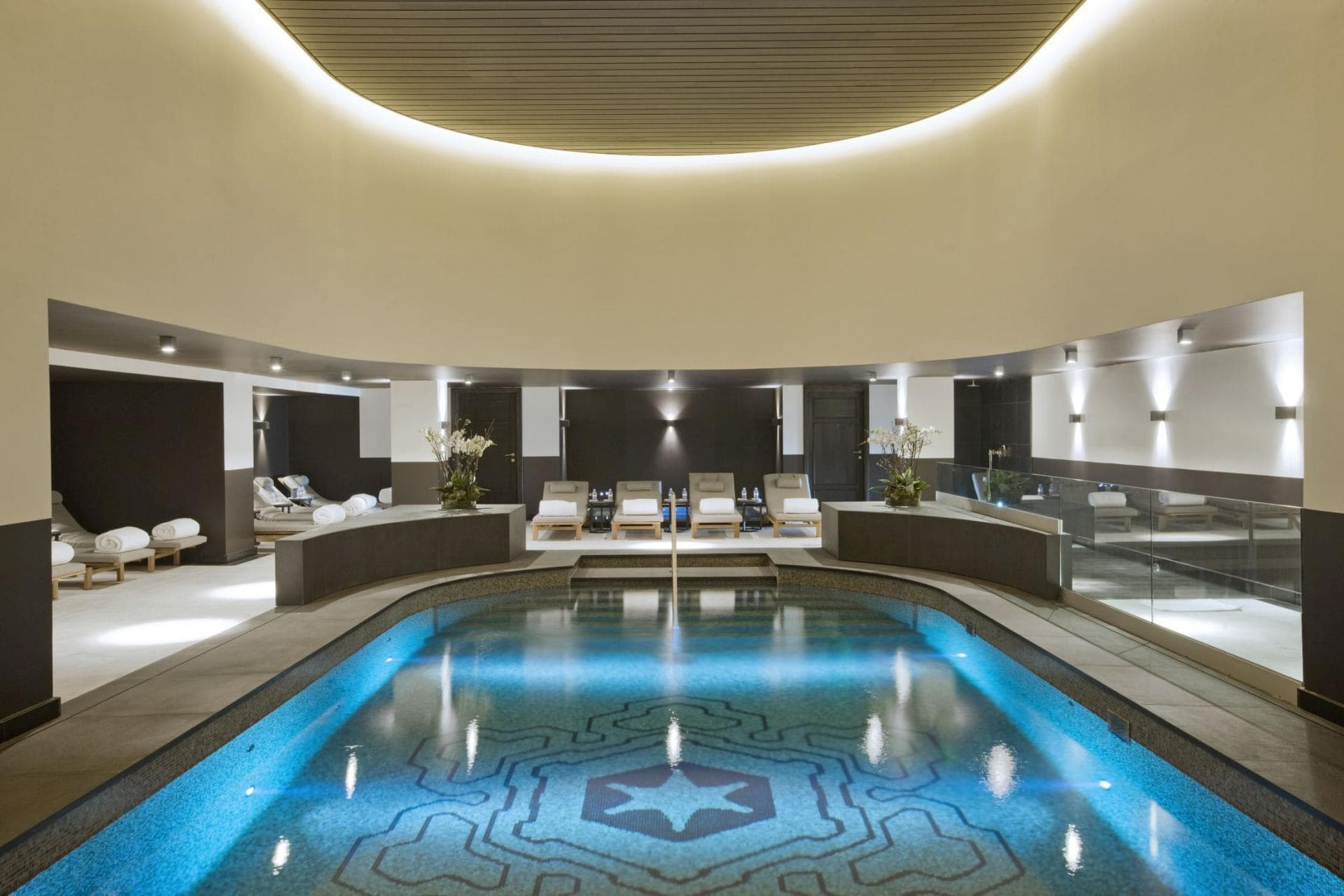 Indoor heated pool with mosaic tiling and poolside lounge seating