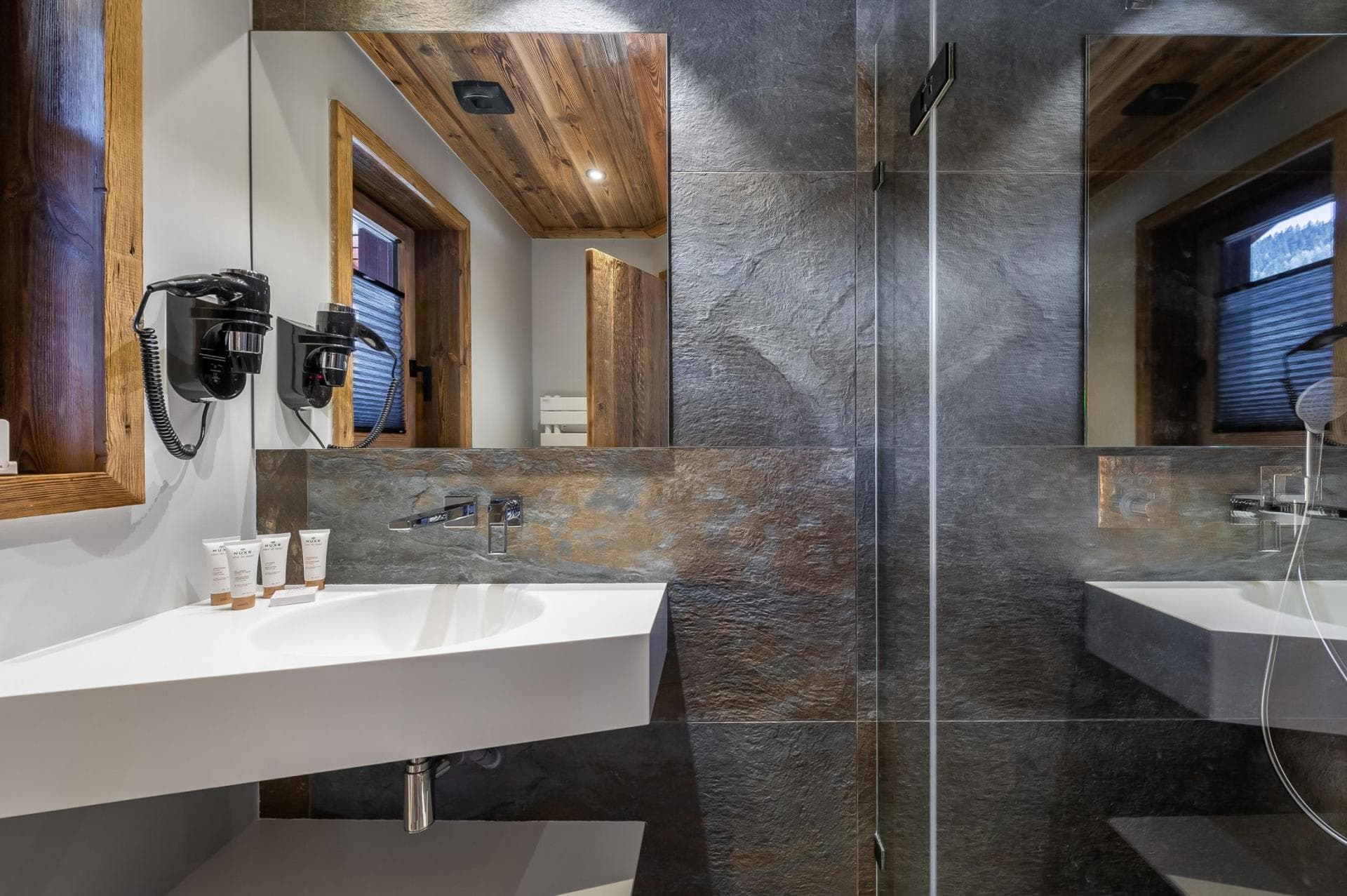 Bathroom with stone tiling, wall-mounted hairdryer, and walk-in shower