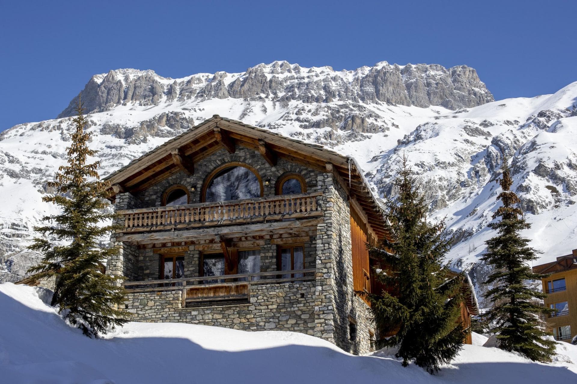 Stone and timber chalet with multiple balconies; mountain backdrop
