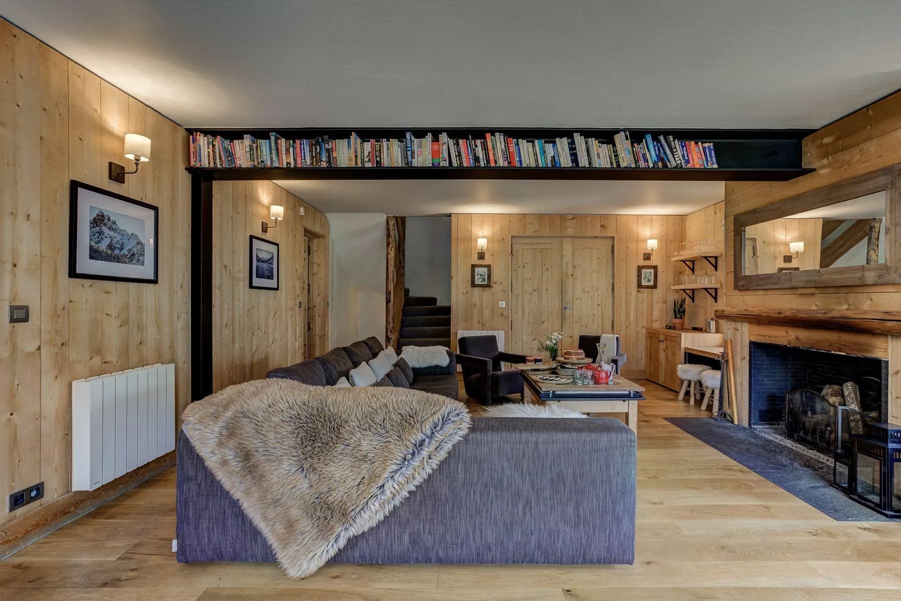 Open-plan living area with timber beams, an open fireplace and bookshelves
