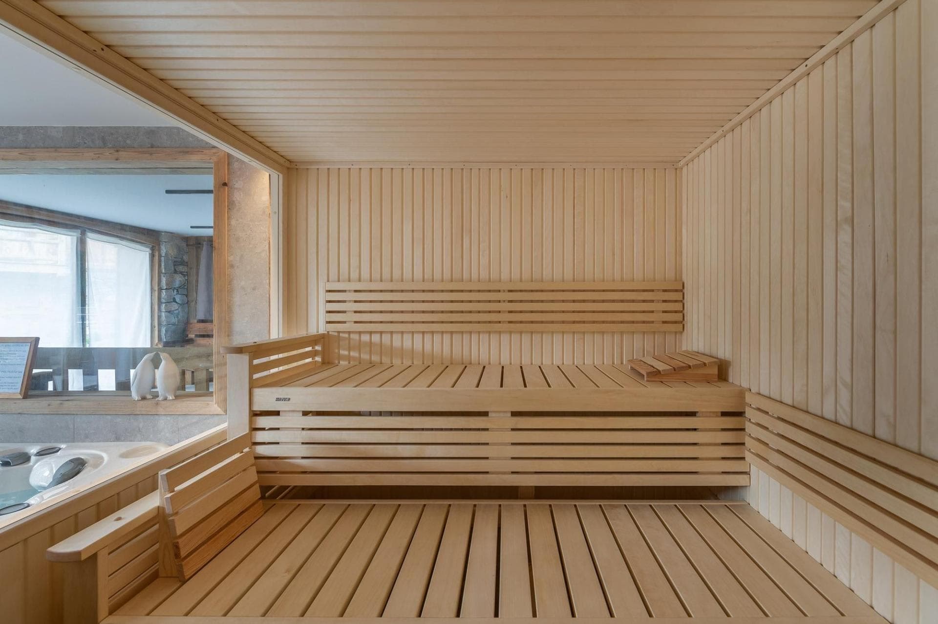 Wood-paneled sauna with tiered seating and adjacent indoor hot tub