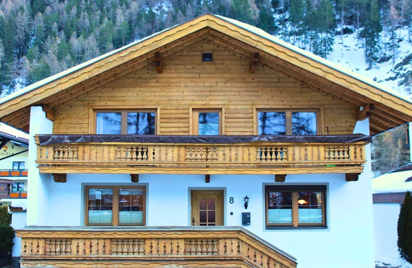 Alpine chalet facade featuring upper-level balcony and mountain forest backdrop