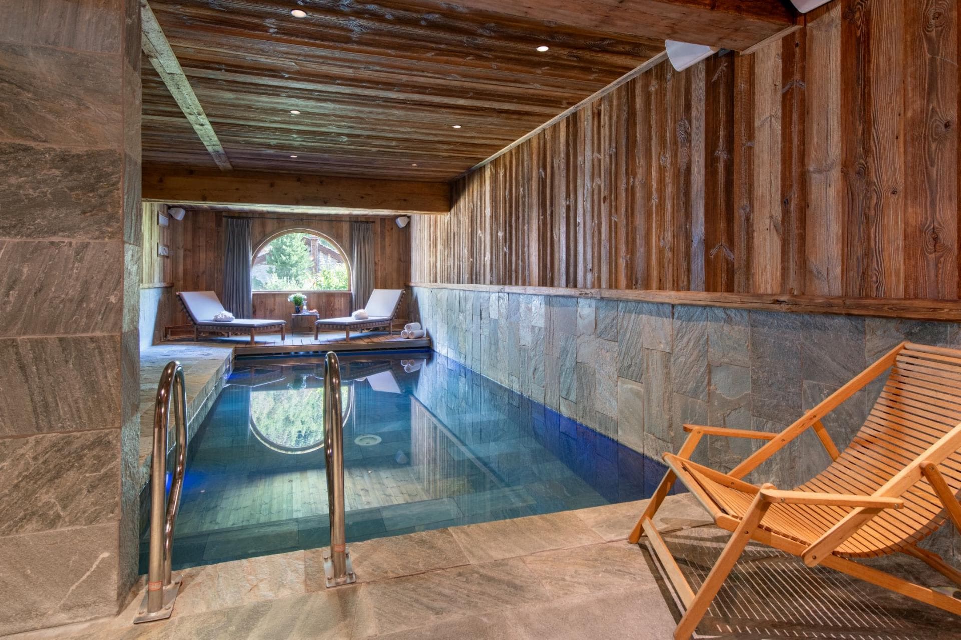 Indoor lap pool with stone tile and poolside lounge seating